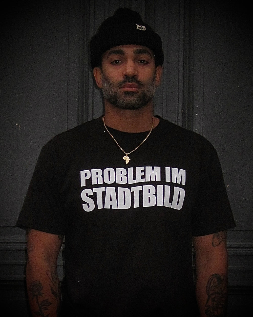 Person mit graumeliertem Bart, Tattoos und Ketten trägt das BBU LAB – PROBLEM IM STADTBILD T-Shirt, frontal fotografiert.